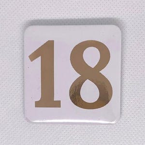 May include: White square with the number 18 in gold foil.