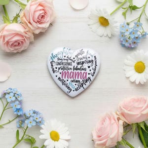 May include: A white heart-shaped decorative item with the word "mama" in pink, surrounded by words like "loving" and "caring." The item is surrounded by pink roses, white daisies, and blue flowers.
