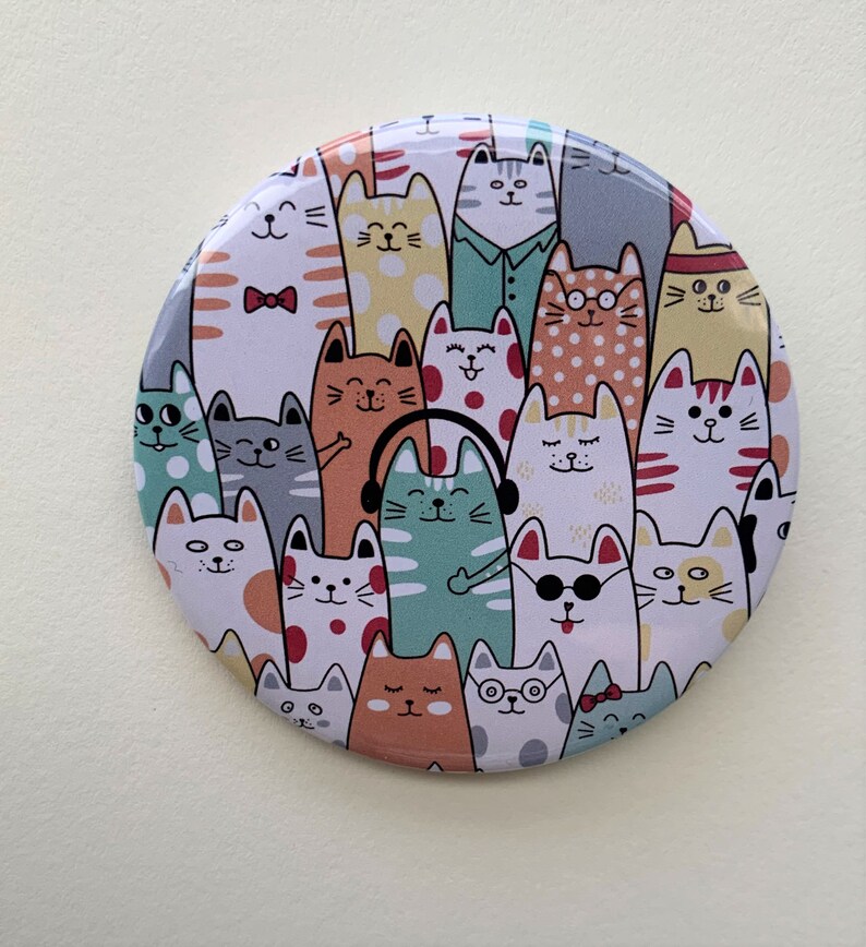 K&ouml;nnte beinhalten: Ein runder Spiegel mit einem farbenfrohen Design von Katzen. Die Katzen sind alle in verschiedenen Farben und haben unterschiedliche Gesichtsausdr&uuml;cke. Einige Katzen tragen Sonnenbrillen, Kopfh&ouml;rer und Fliegen.