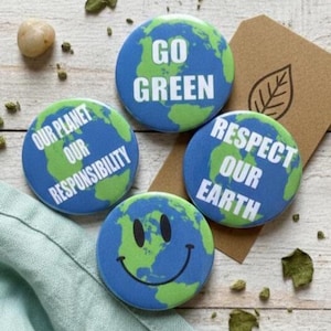 May include: Four circular pin-back buttons featuring a blue and green Earth graphic. One button reads GO GREEN, another says OUR PLANET OUR RESPONSIBILITY, and a third says RESPECT OUR EARTH. The fourth button features a black smiley face on the Earth.