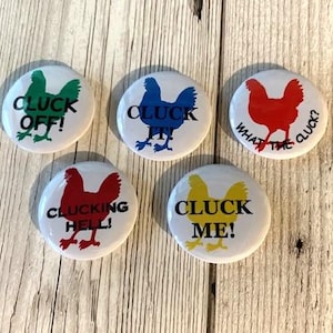 Peut inclure: Cinq boutons ronds blancs avec une silhouette de poulet noire et une phrase humoristique sur le thème du poulet. Les boutons sont vert, bleu, rouge, jaune et rouge. Les phrases sont "Cluck Off!" "Cluck It!" "What the Cluck?" "Cluck Me!" et "Cluckin' Hell!"