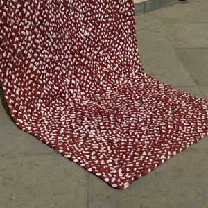 Könnte beinhalten: Ein handgefertigter Teppich mit strukturiertem Muster. Der Teppich hat ein sich wiederholendes Design aus weißen und weinroten Knoten. Der Teppich ist rechteckig und scheint aus einem dicken, strapazierfähigen Material zu bestehen.