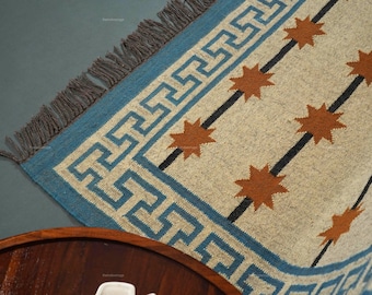 May include: A woven rug with a blue border featuring a geometric pattern. The rug has a beige background with orange starburst designs and black diagonal stripes. The rug has a fringed edge.