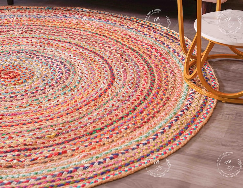 K&ouml;nnte beinhalten: Ein runder, geflochtener Teppich mit Spiralmuster. Der Teppich zeigt eine Mischung aus Farben, darunter Rot, Orange, Rosa, Blau und Gr&uuml;n. Er besteht aus einer Naturfaser und hat ein strukturiertes Aussehen. Der Teppich liegt auf einem Holzboden.