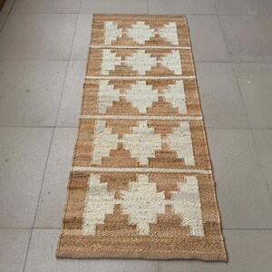 May include: A rectangular runner rug featuring a natural tan jute base with a repeating white geometric diamond pattern. The woven texture is visible throughout the surface, showcasing a series of five distinct diamond shapes aligned vertically.