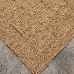 Könnte beinhalten: Ein Naturfaserteppich mit geometrischem Muster. Der Teppich besteht aus einem hellbraunen Material und weist ein sich wiederholendes quadratisches Design auf. Die Textur des Teppichs ist sichtbar, mit einem gewebten Aussehen. Der Teppich liegt auf einer grauen Oberfläche.