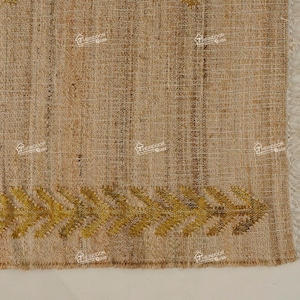 Puede incluir: Primer plano de una alfombra de fibra natural con textura tejida. La alfombra tiene un borde de flecos y un patrón decorativo de hojas amarillas a lo largo del borde inferior.