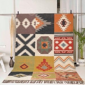 May include: A colorful, geometric patterned rug with a patchwork design. The rug features squares of brown, black, orange, and cream with various Southwestern-inspired motifs. The rug has a fringed edge and is displayed on a white background.
