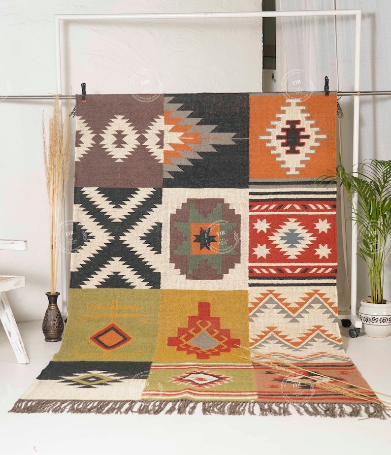 May include: A colorful, geometric patterned rug with a patchwork design. The rug features squares of brown, black, orange, and cream with various Southwestern-inspired motifs. The rug has a fringed edge and is displayed on a white background.