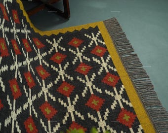 May include: A patterned rug with a dark gray background and a repeating diamond design in red, white, and green. The rug has a yellow border and gray fringe.