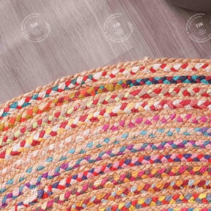 K&ouml;nnte beinhalten: Nahaufnahme eines runden, geflochtenen Jute-Teppichs mit bunten Streifen. Der Teppich hat eine nat&uuml;rliche beige Basis mit B&auml;ndern in Rot, Blau, Gelb und Rosa. Die Textur des Teppichs ist sichtbar und zeigt die gewebte Konstruktion.