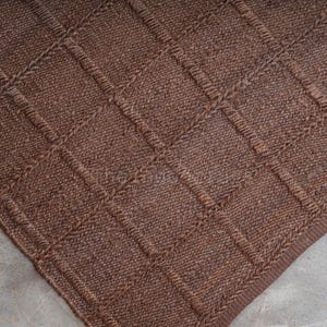 May include: A dark brown woven rug featuring a raised grid pattern of squares. The texture is dense and uniform, created by thick, interlaced fibers that form a consistent geometric design across the entire surface of the rectangular floor covering.