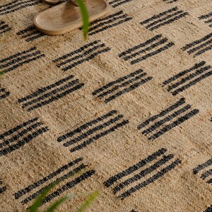 May include: A natural fiber rug with a woven texture and a repeating pattern of black stripes. The rug is beige and has a simple, geometric design. The rug is suitable for indoor use.