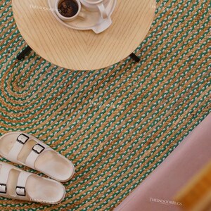 Puede incluir: Vista a&eacute;rea de una alfombra redonda de yute con un dise&ntilde;o verde y beige. Una peque&ntilde;a mesa de madera con un juego de caf&eacute; encima. Sandalias blancas con hebillas negras sobre la alfombra.