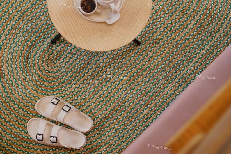 Puede incluir: Vista a&eacute;rea de una alfombra redonda de yute con un dise&ntilde;o verde y beige. Una peque&ntilde;a mesa de madera con un juego de caf&eacute; encima. Sandalias blancas con hebillas negras sobre la alfombra.