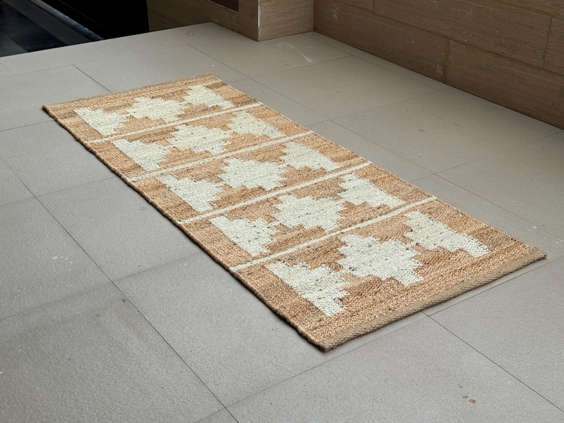 May include: A rectangular runner rug featuring a natural tan jute base with a repeating white geometric diamond pattern. The woven texture is visible throughout the surface, showcasing a series of five distinct diamond shapes aligned horizontally.