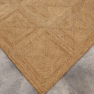 Könnte beinhalten: Nahaufnahme eines Naturfaserteppichs mit geometrischem Muster. Der Teppich besteht aus gewebtem, hellbraunem Material. Das Muster zeigt eine Reihe von Rautenformen. Der Teppich liegt auf einer grauen Oberfläche.