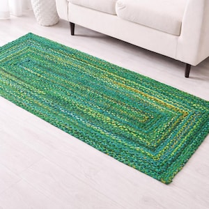 Könnte beinhalten: Ein rechteckiger grüner Teppich mit geflochtener Textur. Der Teppich hat einen Rand und liegt auf einem hellen Holzboden. Der Teppich befindet sich in der Nähe eines weißen Sofas und eines kleinen Beistelltisches mit Marmorplatte.