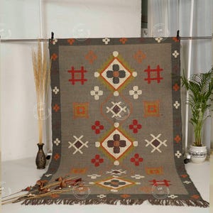 May include: A rectangular gray rug with geometric patterns in red, orange, white, and brown. The rug has a dark gray border and fringe along the bottom edge. The design includes diamond and cross shapes.