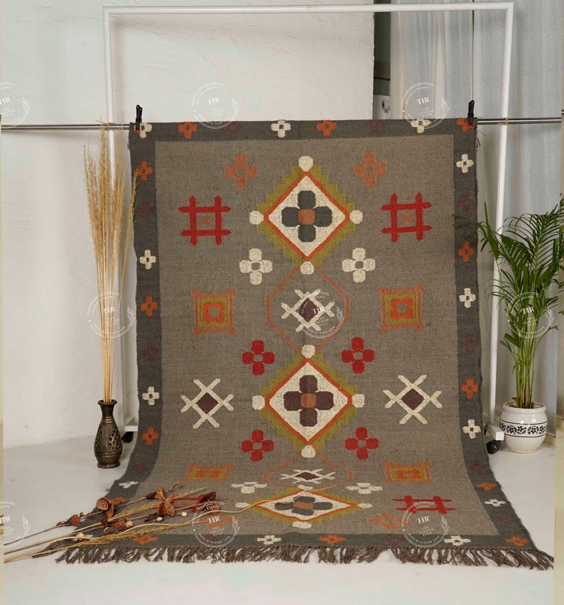May include: A rectangular gray rug with geometric patterns in red, orange, white, and brown. The rug has a dark gray border and fringe along the bottom edge. The design includes diamond and cross shapes.