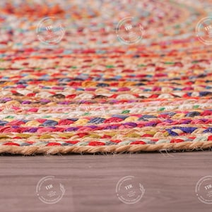 K&ouml;nnte beinhalten: Nahaufnahme eines runden, geflochtenen Jute-Teppichs mit einem farbenfrohen Streifenmuster. Der Teppich weist eine Mischung aus roten, rosa, orangefarbenen, gelben, blauen und violetten Farbt&ouml;nen auf. Der Teppich liegt auf einer Holzoberfl&auml;che.