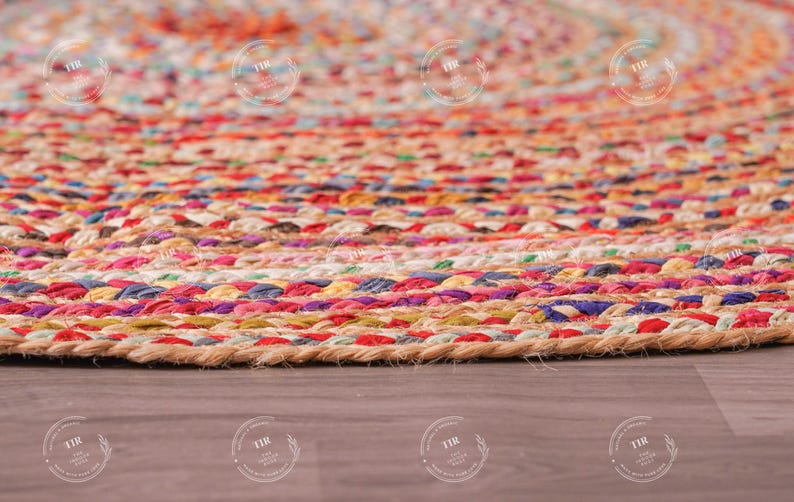 K&ouml;nnte beinhalten: Nahaufnahme eines runden, geflochtenen Jute-Teppichs mit einem farbenfrohen Streifenmuster. Der Teppich weist eine Mischung aus roten, rosa, orangefarbenen, gelben, blauen und violetten Farbt&ouml;nen auf. Der Teppich liegt auf einer Holzoberfl&auml;che.
