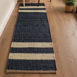 Op de afbeelding: Een marineblauw en beige gestreept loperkleed. Het rechthoekige kleed is gemaakt van geweven materiaal. Twee brede beige strepen zijn te zien op de marineblauwe achtergrond. Het kleed ligt op een houten vloer.