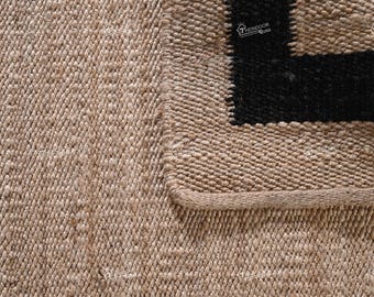 May include: Close-up of a natural fibre rug with a black and white geometric pattern. The rug is woven with a textured, slightly rough surface.