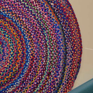 May include: A colorful, round braided rug with a spiral pattern. The rug features a mix of vibrant colors including blue, pink, yellow, and orange. The rug is made of woven fabric and is suitable for home decor.
