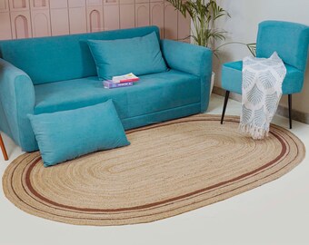 May include: A teal sofa with matching throw pillows and a teal armchair are arranged on a light brown oval jute rug with a dark brown border. A white throw blanket with a leaf pattern is draped over the chair.