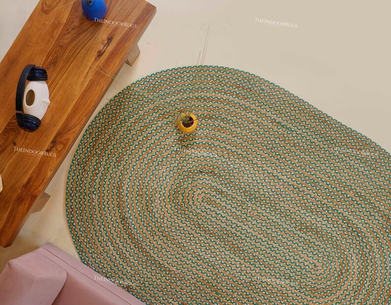 Puede incluir: Una alfombra ovalada con base de yute natural y borde verde. La alfombra est&aacute; colocada sobre un suelo de color claro. Una mesa de madera y un sof&aacute; rosa son parcialmente visibles. La alfombra es un art&iacute;culo de decoraci&oacute;n del hogar.
