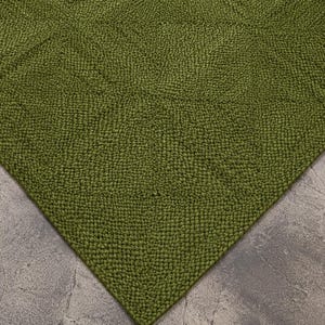 Op de afbeelding: Een olijfgroen kleed met een dicht, getextureerd, handgeknoopt weefsel. Het oppervlak vertoont een subtiel geometrisch patroon gevormd door de rangschikking van de individuele lussen, wat zorgt voor een consistente, tactiele en uniforme uitstraling.