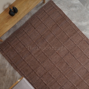 May include: A rectangular brown rug featuring a raised grid pattern of woven lines. The surface has a textured appearance with a consistent square design throughout. The text Theindoorrugs is visible in the center of the brown rug.