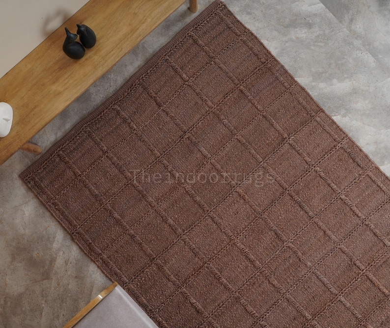 May include: A rectangular brown rug featuring a raised grid pattern of woven lines. The surface has a textured appearance with a consistent square design throughout. The text Theindoorrugs is visible in the center of the brown rug.