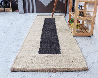 May include: A natural fiber rug with a black stripe down the center. The rug is beige and has a woven texture.