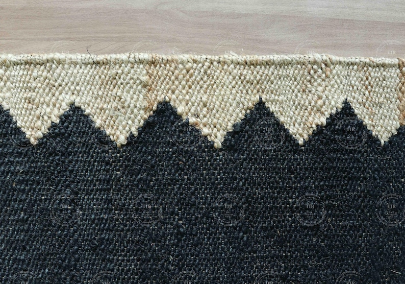 Op de afbeelding: Close-up van een geweven vloerkleed met een geometrisch bergontwerp. Het vloerkleed heeft een zwarte basis met een cr&egrave;mekleurige zigzagrand. De textuur van het vloerkleed is zichtbaar, met de natuurlijke vezels.