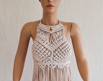 May include: A beige crochet halter top with fringe detailing. The top has a small, colourful bead at the centre of the neckline.