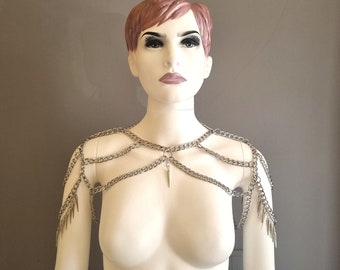 Op de afbeelding: Een zilveren kettinghemd schouderstuk met hangende spikes. Het kettinghemd is gelaagd en heeft een delicate hanger die in het midden hangt.
