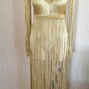 Puede incluir: Un vestido de crochet dorado con cuello alto y mangas largas. El vestido tiene un detalle de flecos y est&aacute; hecho de un hilo suave y ligero.