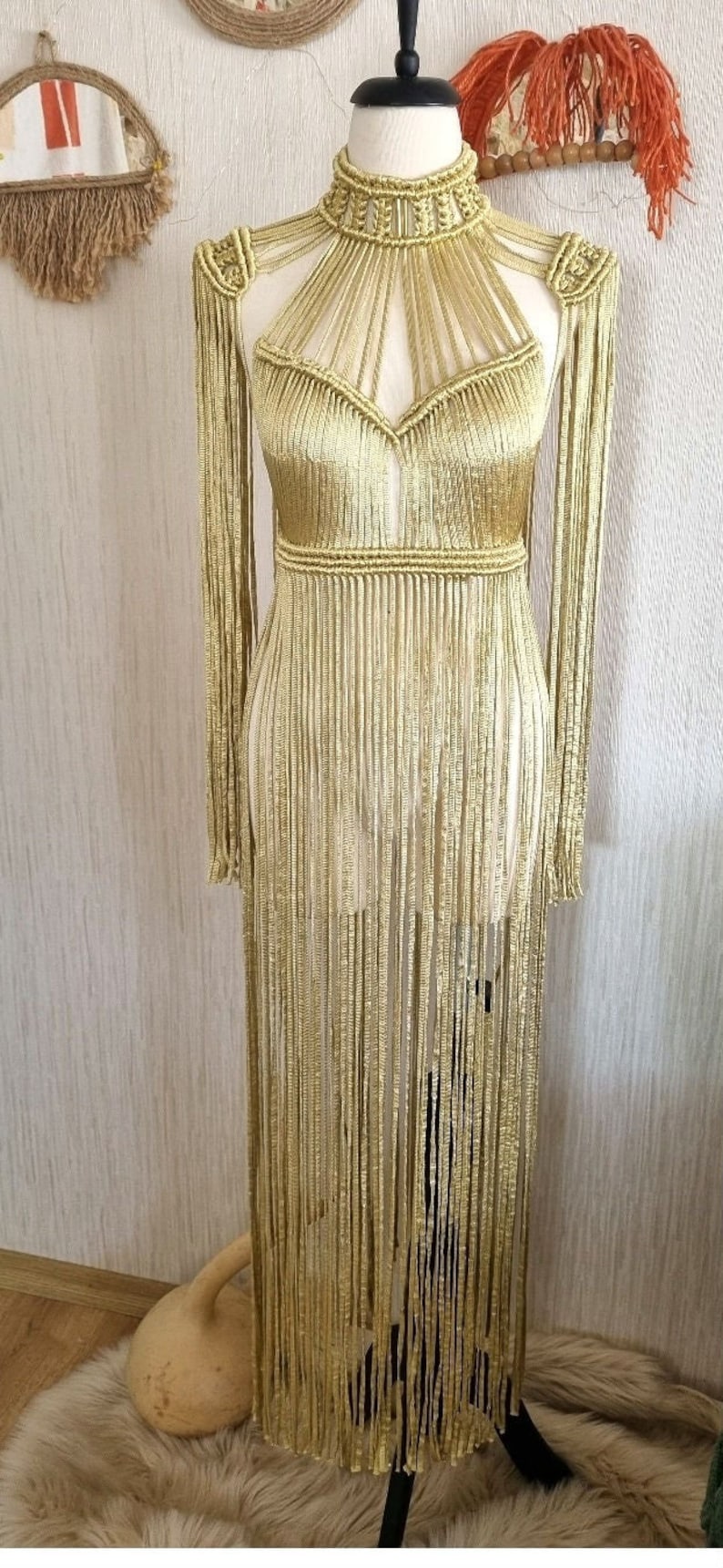 Puede incluir: Un vestido de crochet dorado con cuello alto y mangas largas. El vestido tiene un detalle de flecos y est&aacute; hecho de un hilo suave y ligero.
