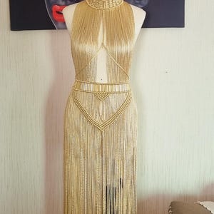 May include: A gold halter top and skirt made of long, thin strands of fabric. The top has a plunging neckline and the skirt is floor-length.