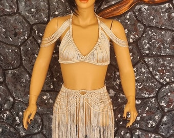 May include: Beige crochet top and skirt set with fringe detailing. The top has a halter neckline and the skirt is a mini length.