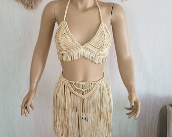 May include: A cream-coloured crocheted bikini top and skirt set with fringe detailing. The set is made of a soft, lightweight material and is perfect for a beach day or a summer festival.