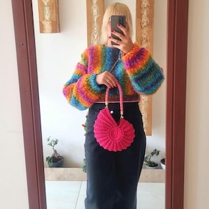 May include: A rainbow striped crocheted sweater with long sleeves and a pink crocheted heart-shaped purse with a gold chain strap.