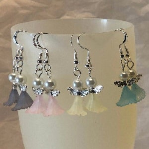 Puede incluir: Un conjunto de ocho pares de pendientes colgantes con un peque&ntilde;o dise&ntilde;o de &aacute;ngel con un acento de perla. Los &aacute;ngeles est&aacute;n hechos de pl&aacute;stico transl&uacute;cido y vienen en una variedad de colores pastel, incluyendo lavanda, rosa, blanco, azul claro, amarillo, morado claro, naranja y azul.