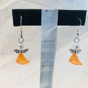 Puede incluir: Un par de pendientes de &aacute;ngel de plata con alas naranjas y una perla blanca. Los pendientes miden aproximadamente 2,5 cm de largo.