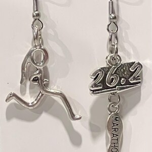 May include: A pair of silver earrings featuring a runner and the text "26.2 Marathon" hanging from them.