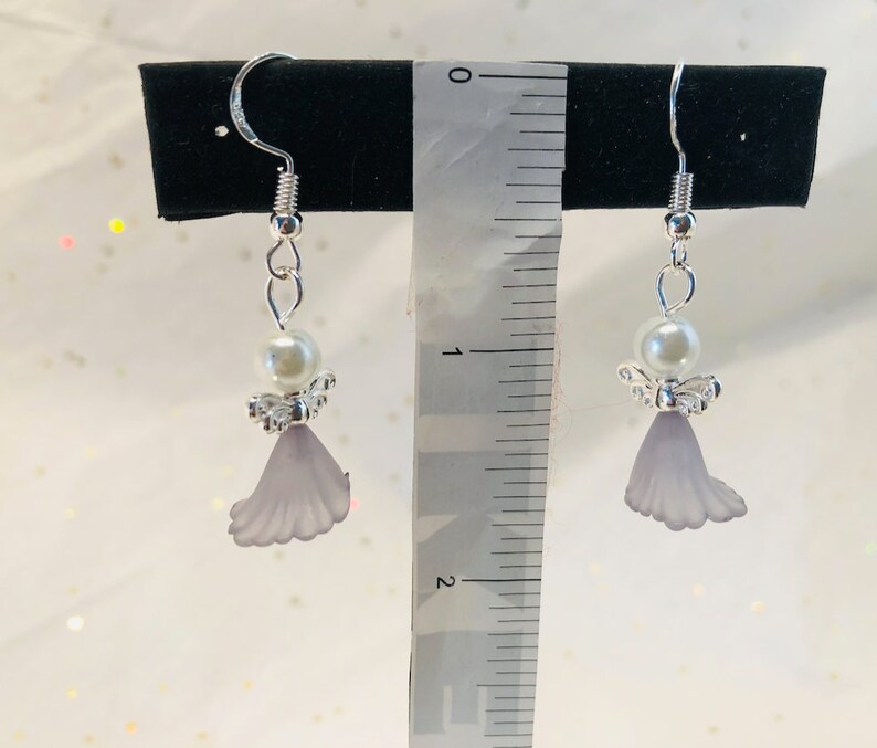 Puede incluir: Un par de pendientes de &aacute;ngel de plata con una perla blanca y un dije en forma de flor lavanda. Los pendientes miden aproximadamente 2,5 cm de largo.