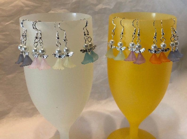 Puede incluir: Un conjunto de ocho pares de pendientes colgantes con un peque&ntilde;o dise&ntilde;o de &aacute;ngel con un acento de perla. Los &aacute;ngeles est&aacute;n hechos de pl&aacute;stico transl&uacute;cido y vienen en una variedad de colores pastel, incluyendo lavanda, rosa, blanco, azul claro, amarillo, morado claro, naranja y azul.