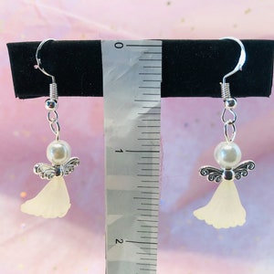 Puede incluir: Un par de pendientes de &aacute;ngel colgantes de plata con cuentas de perlas blancas y alas de &aacute;ngel blancas transl&uacute;cidas. Los pendientes miden aproximadamente 5 cm de largo.